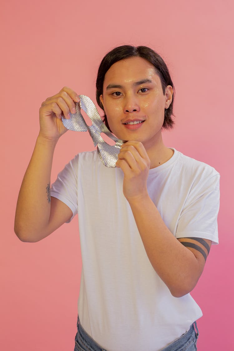 Positive Asian Man Removing Fabric Mask Sheet In Studio