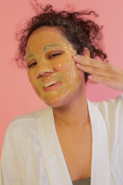 Cheerful ethnic woman applying rejuvenating mask sheet on face