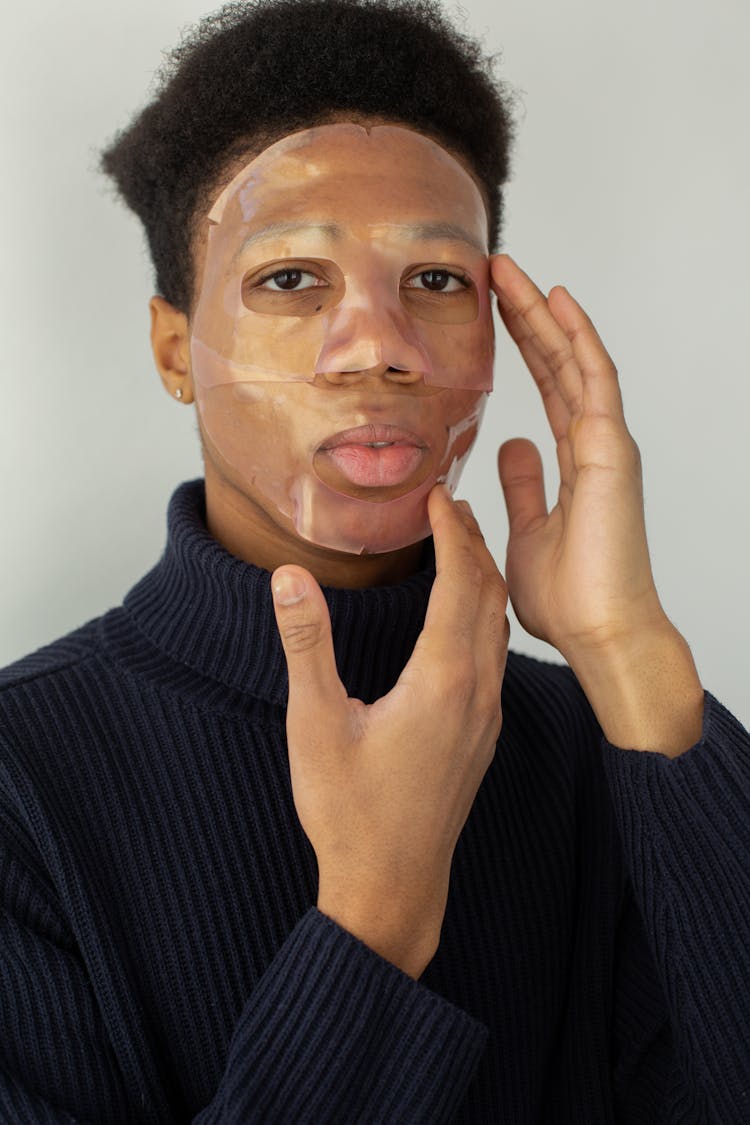 Unemotional Black Man Applying Cosmetic Face Mask