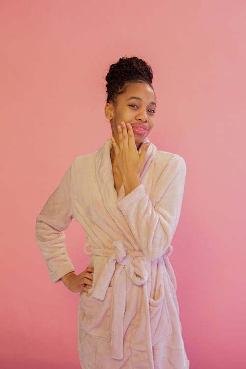 Cheerful black woman in bathrobe touching face gently