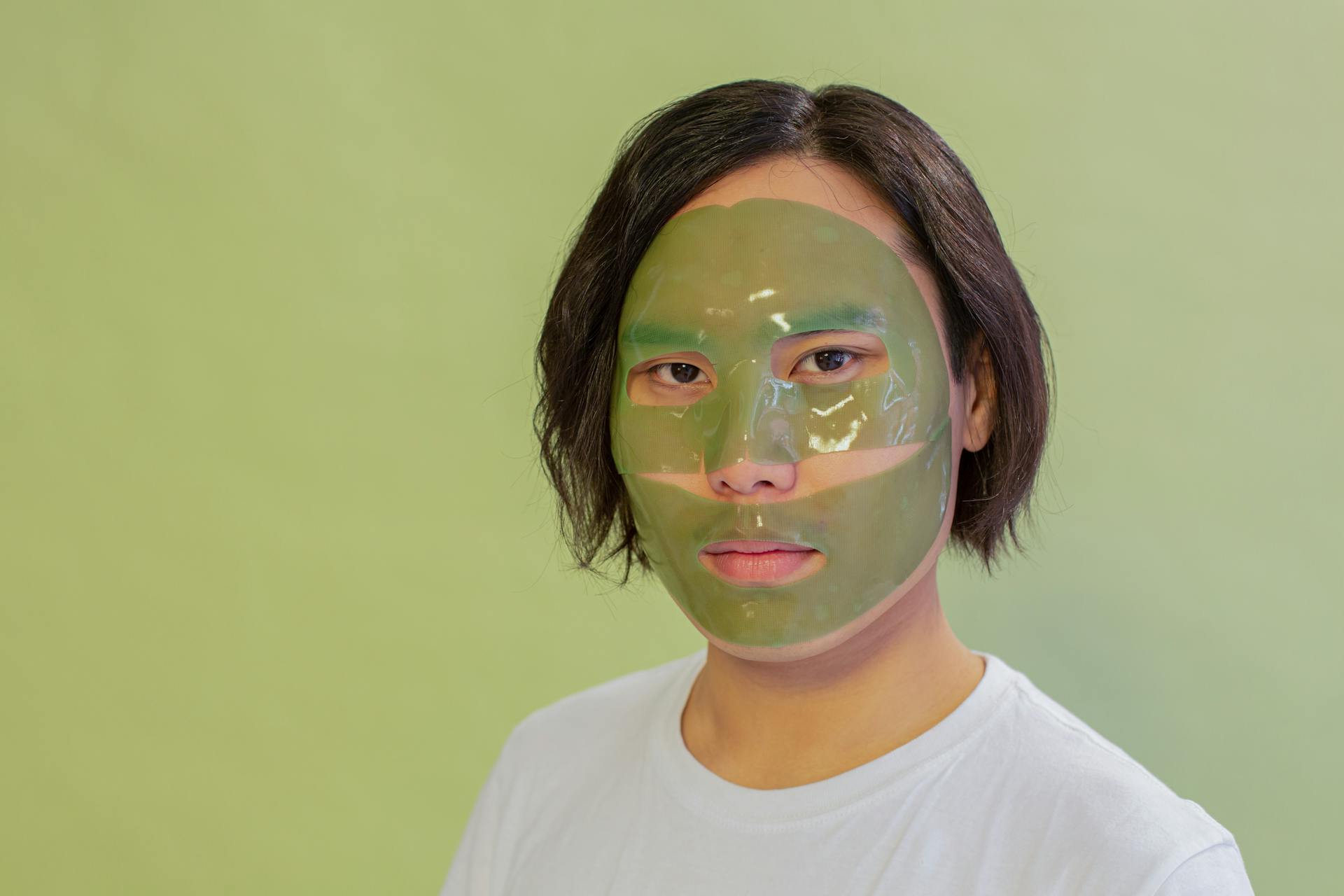 Calm Asian man with facial mask during cosmetic procedure