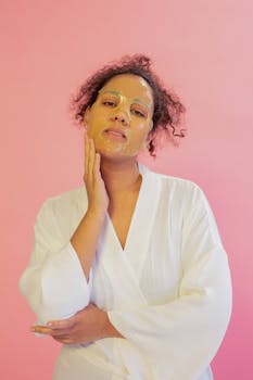 Woman in a bathrobe applying facial mask, promoting skincare.