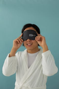 A young adult wearing a sleep mask and bathrobe against a blue background. Ideal image for relaxation themes.