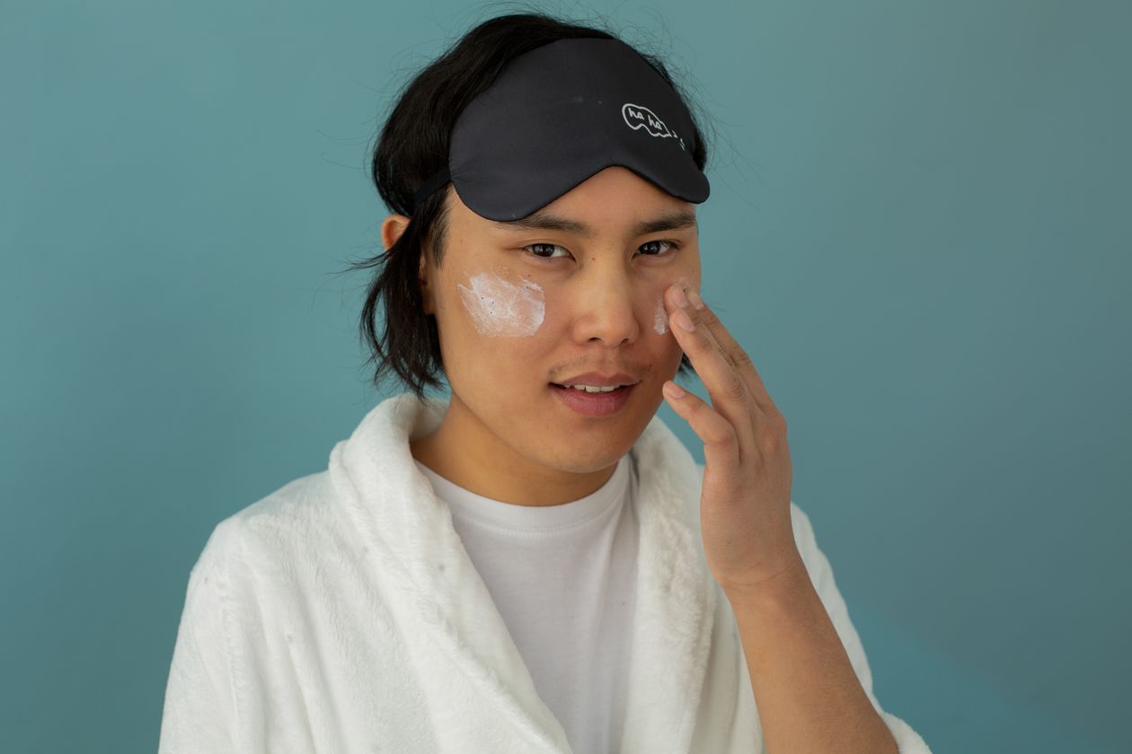 Man applying skincare cream in a robe, focusing on facial care routine