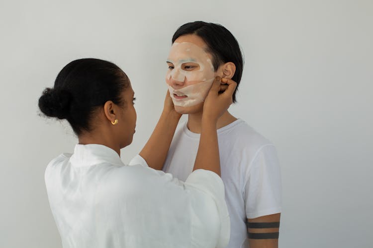 Black Cosmetologist Applying Moisturizing Mask On Face Of Asian Client