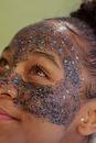 Crop black female adolescent looking up with exfoliating mask on cheeks and forehead with stars and shiny particles on green background