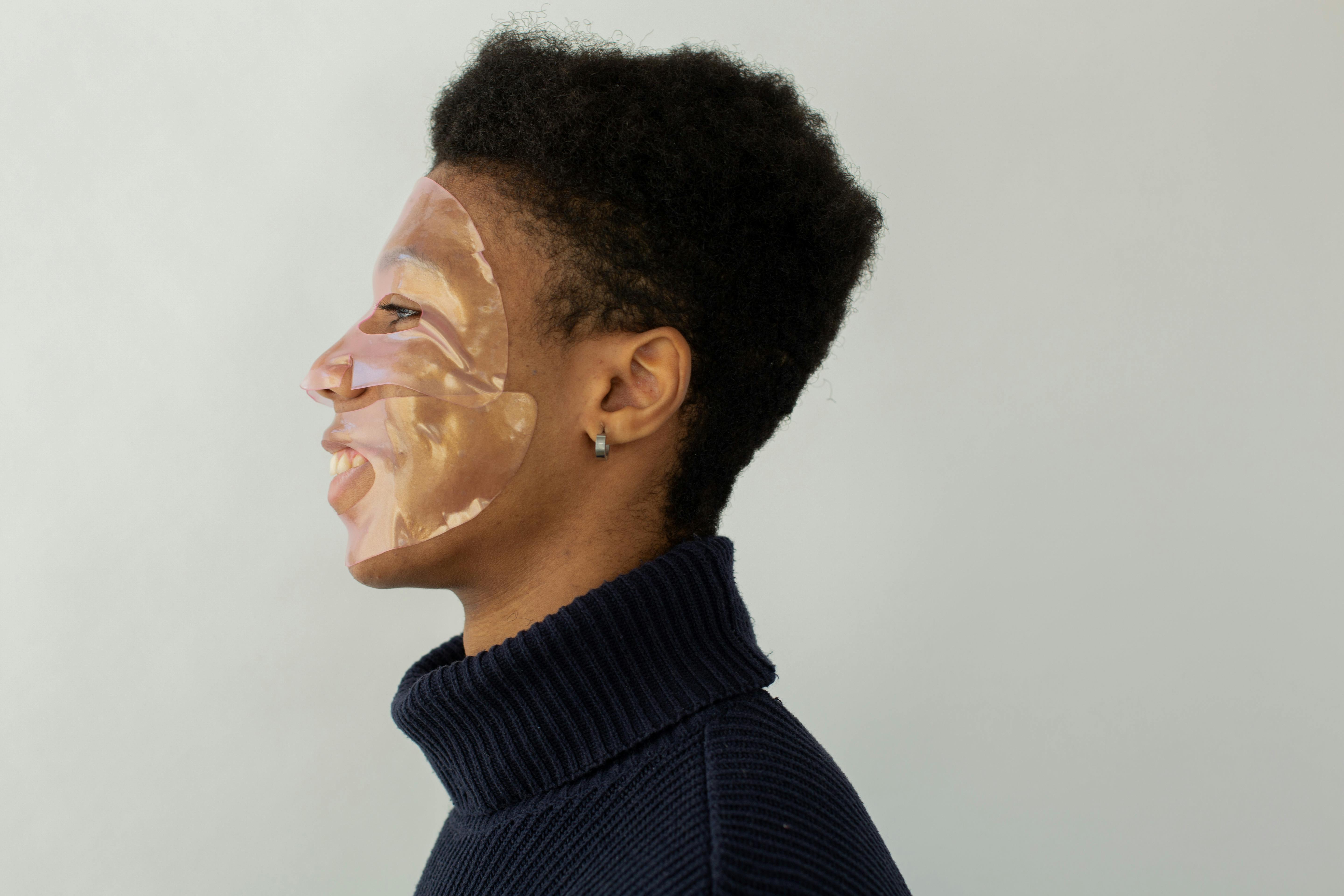 Studio portrait of a man wearing a facial mask, side profile with a light background.