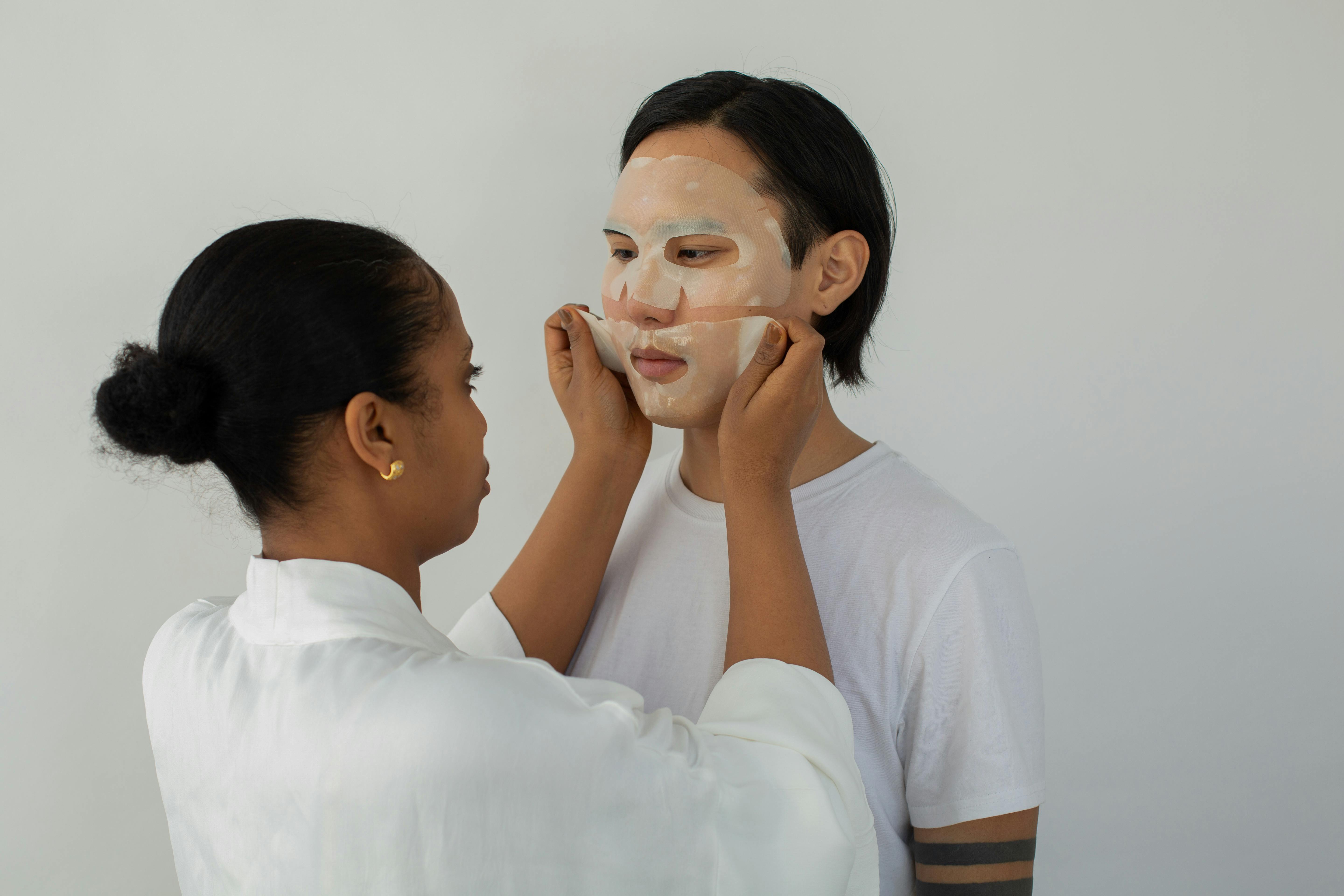 ethnic beautician applying sheet mask on face of asian client