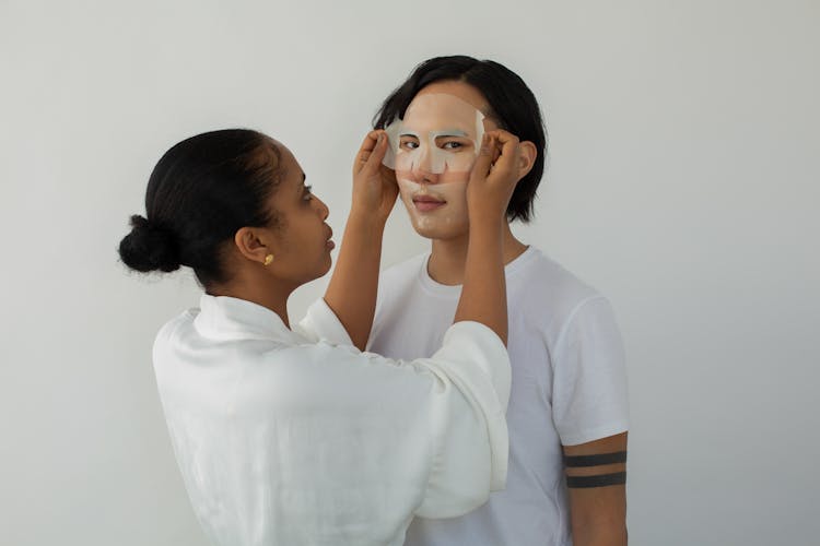 Black Cosmetologist Applying Sheet Mask On Face Of Ethnic Client