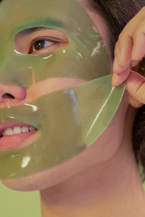 Crop contemplative ethnic male with brown eye removing seaweed mask from face while looking away