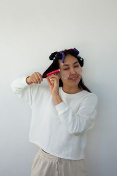 Young smiling ethnic female with eye patches on face curling hair on curlers while looking away