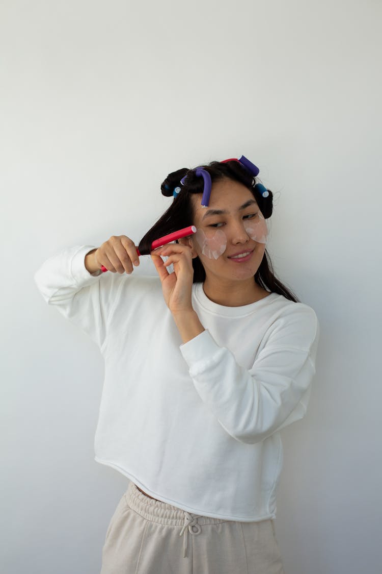 Asian Woman Curling Hair On Rollers On Light Background