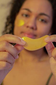 Soft focus of African American young female demonstrating eye patch in hands and looking at camera during skincare routine on beige background