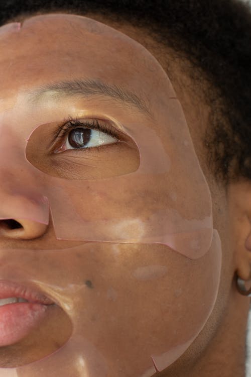 Crop anonymous young African American male with moisturizing cosmetic mask applied on face for daily beauty procedure in light studio