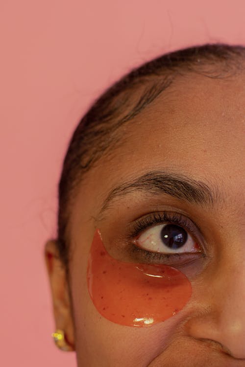 Crop unrecognizable African American female model with eye patch on face standing on pink background during skincare procedure in studio
