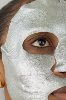 Close-up of a woman's face with a silver sheet mask for skincare routine.