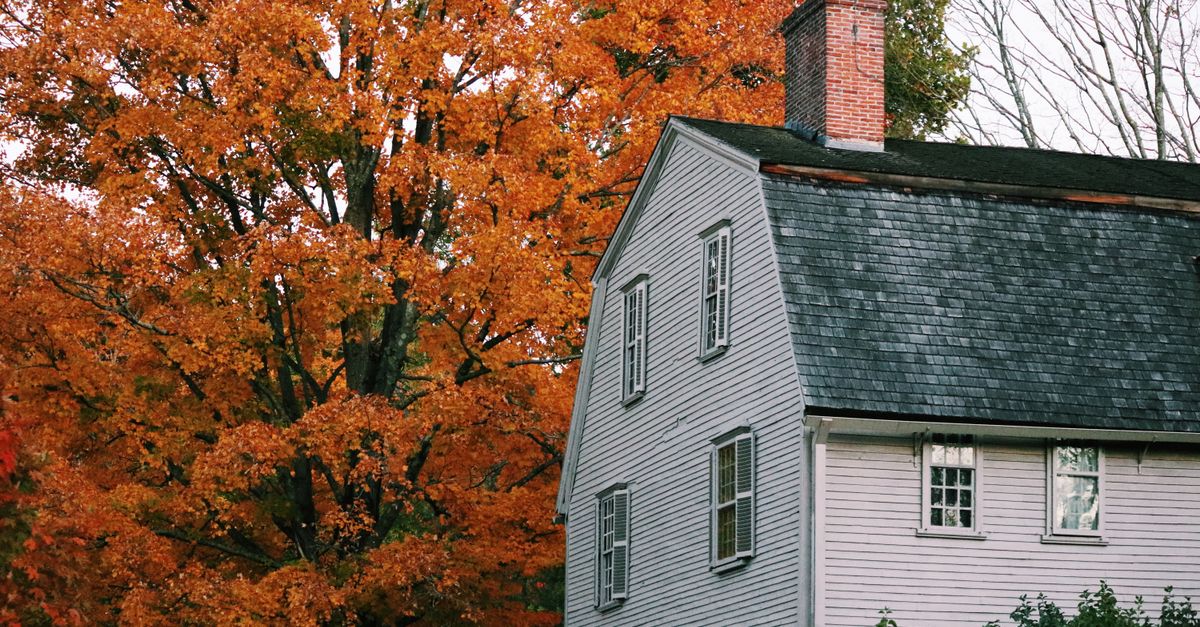 A historic New England house framed by autumn trees.
