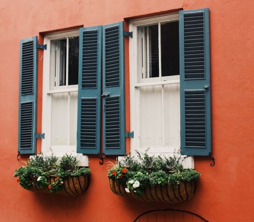 Free Close-up of a rustic house exterior with vibrant shutters and decorative flowerpots against a red wall. Stock Photo