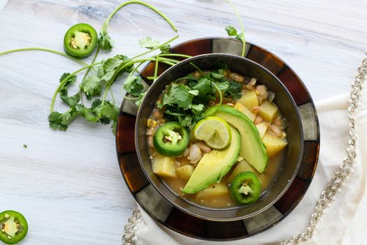 Top view of a colorful vegetable soup garnished with avocado, jalapeño, and cilantro.