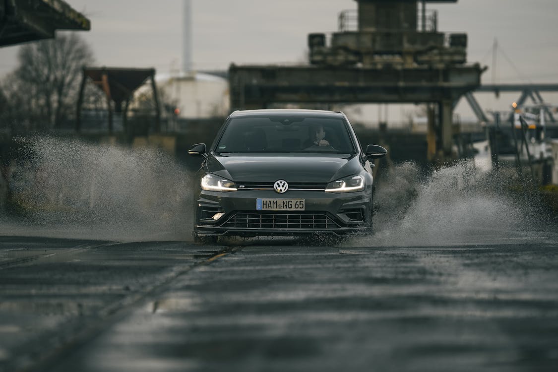 Contemporary black car driving on wet asphalt road and splashing water puddles on gloomy day in suburb