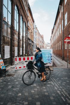 Woman standing with bicycle in a charming Danish alley. Urban lifestyle captured elegantly.