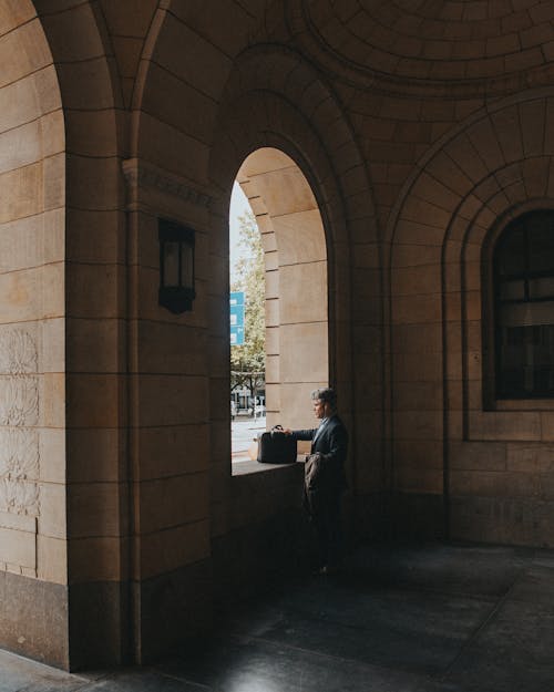 Elegant Man Standing with His Briefcase Next to a Window of an Old Building with Arches 