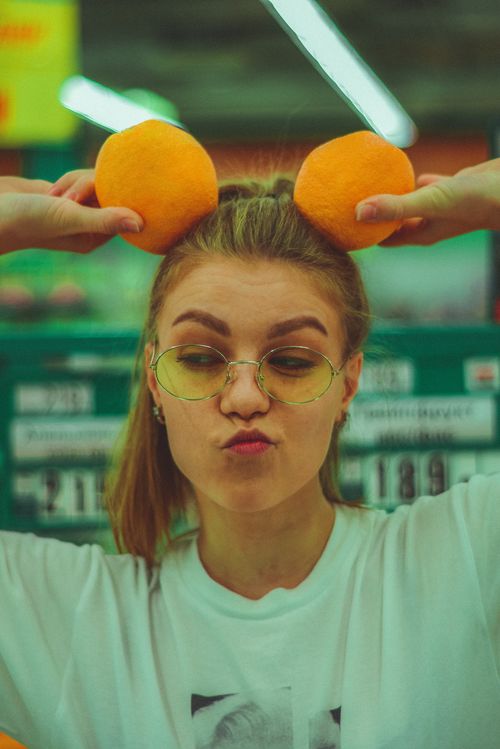 Free Trendy woman in glasses posing with oranges on her head in a playful setting. Stock Photo