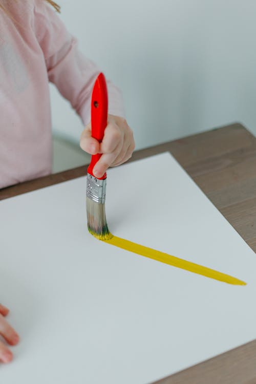 A Person Holding a Paint Brush on a White Surface with Yellow Paint