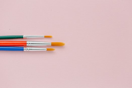 Three vibrant paintbrushes on a pink canvas providing ample copy space.