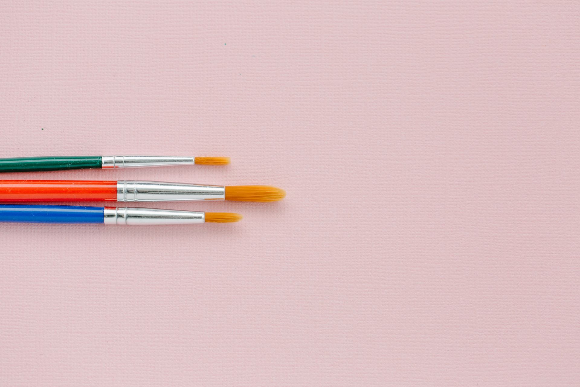 Three vibrant paintbrushes on a pink canvas providing ample copy space.