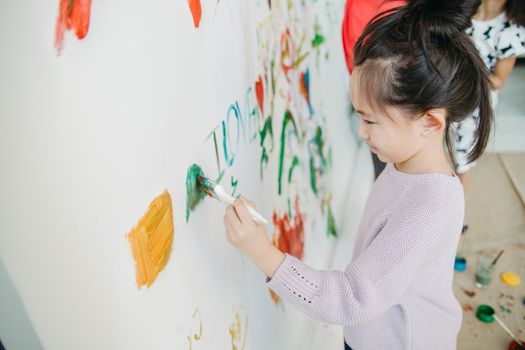 A young girl creatively painting on a wall using a brush, showcasing artistic expression.