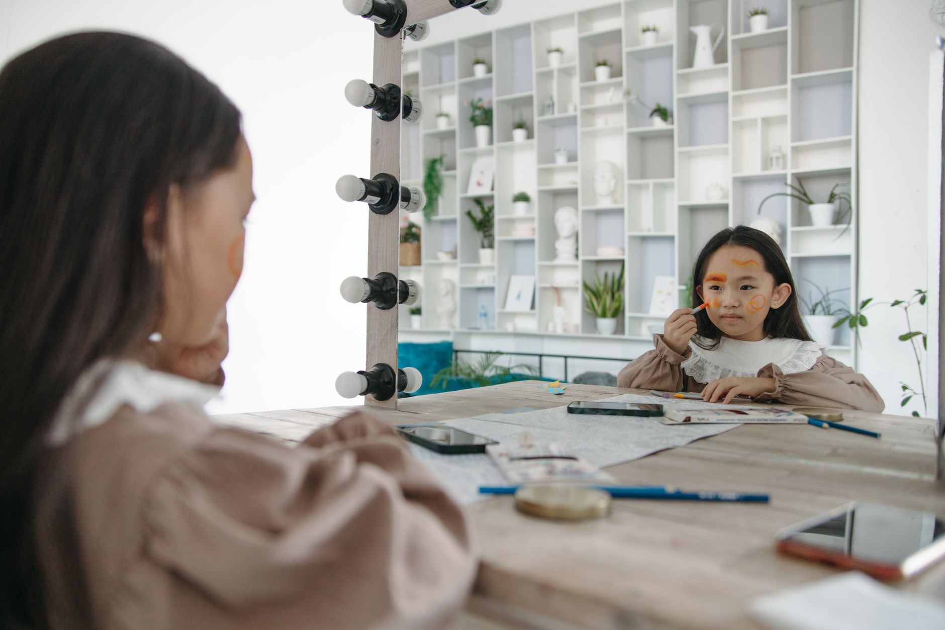 A young girl applies face paint while looking at her reflection in a vanity mirror. A young girl applies face paint while looking at her reflection in a vanity mirror.