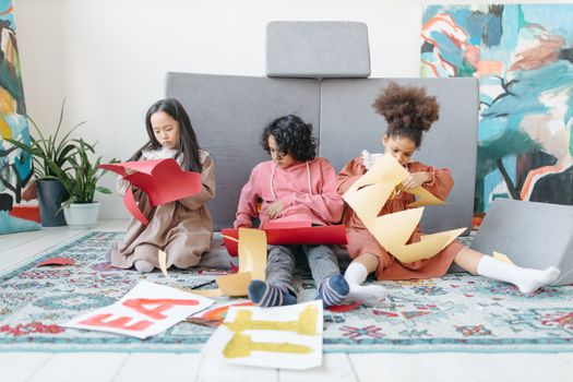 Three children creating art with colored paper indoors, showcasing teamwork and creativity.