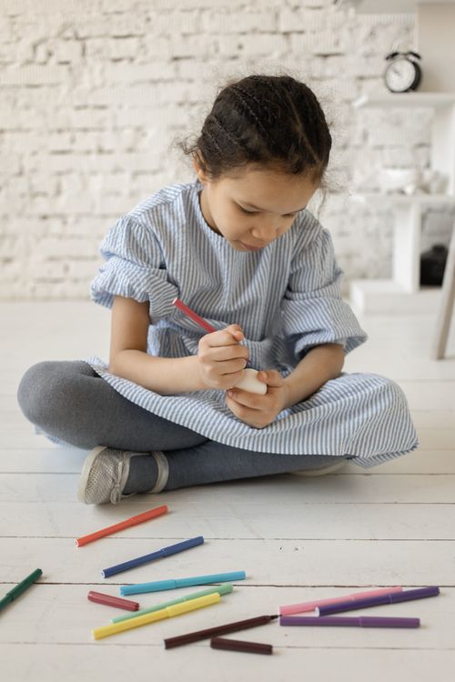 Free Young girl sitting on the floor drawing with colorful pencils in a cozy room. Stock Photo