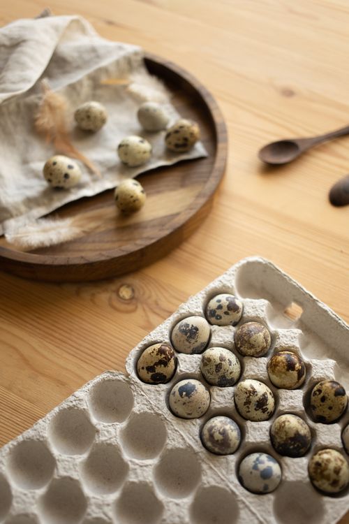Free A selection of quail eggs displayed on a wooden surface with a carton and round tray. Stock Photo