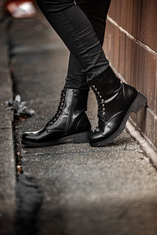 Free A close-up shot of black leather boots worn by a person on an urban sidewalk, showcasing fashion and style. Stock Photo