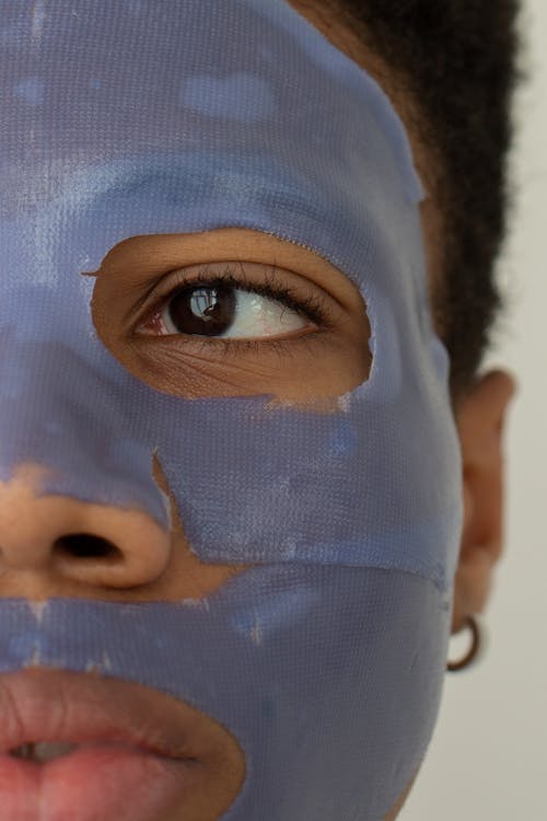 Free Crop unrecognizable young African American male wearing moisturizing facial mask for skincare routine looking away while standing on white background Stock Photo
