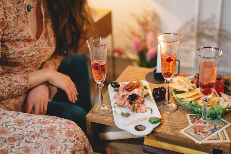 Woman Sitting By Table With Cocktails And Food Platt