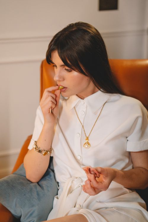 Free A brunette woman in a white dress enjoying a snack while sitting comfortably indoors. Stock Photo