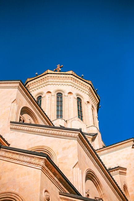 From below of aged stone cathedral with ornamental details and cross shaped windows located in city on sunny day against cloudless blue sky