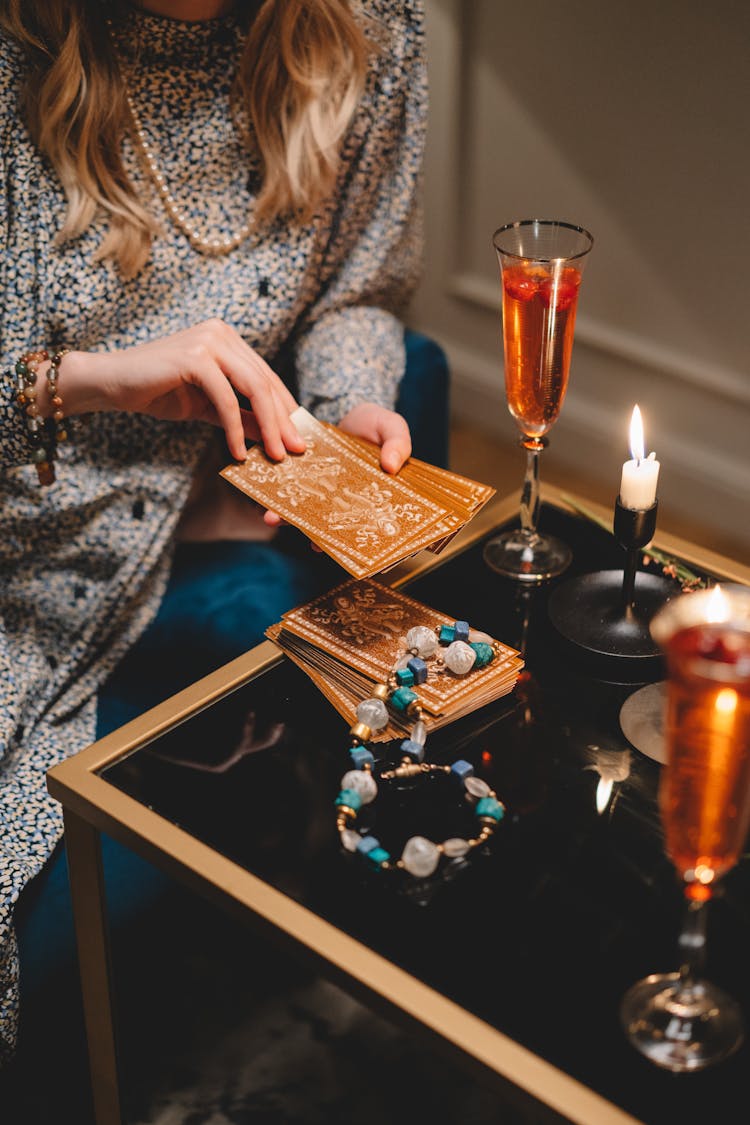 Close-up Of Woman Holding A Deck Of Tarot Cards And Sitting At A Table With Champagne Glasses