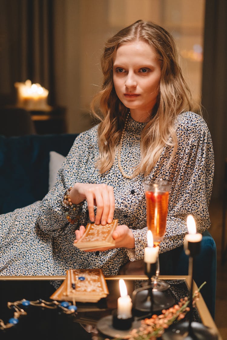 Woman Sitting On A Couch In Front Of A Table With Candles And A Champagne Glass Holding A Deck Of Cards 