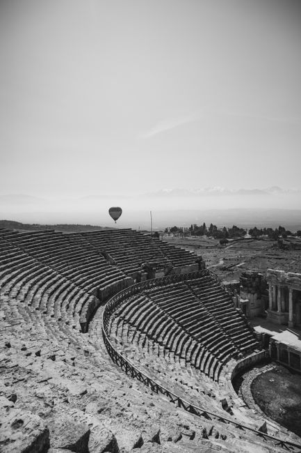 Black and white photo of a hot air balloon above an ancient Roman theatre.
