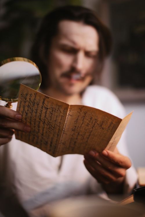 Free Adult man examining a vintage handwritten letter using a magnifying glass, evoking a retro and historical vibe. Stock Photo