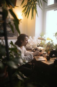 A man enjoying a quiet moment with a book at a cozy, plant-filled home office.