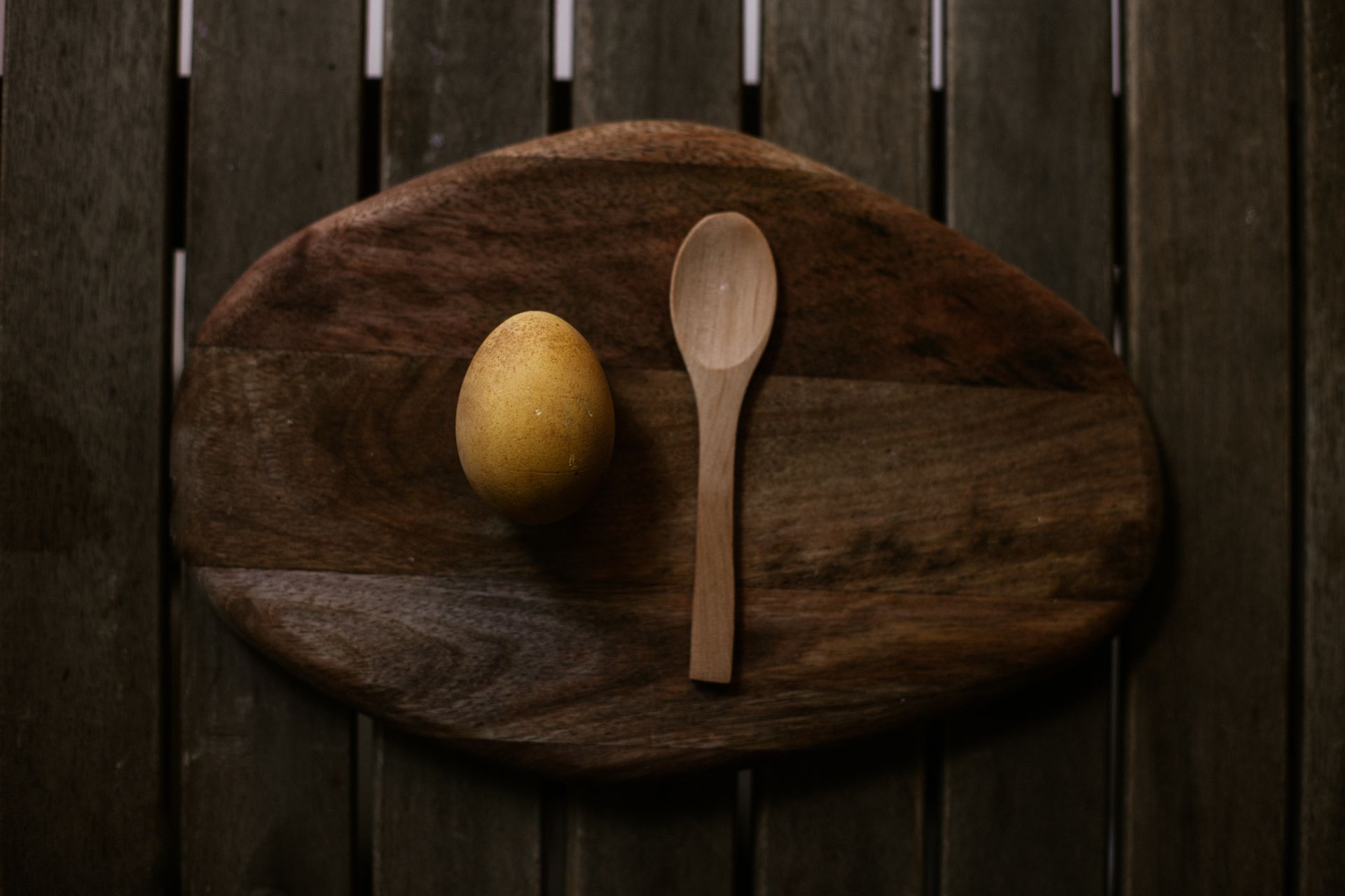 A yellow egg and wooden spoon on an oval cutting board in warm natural lighting.