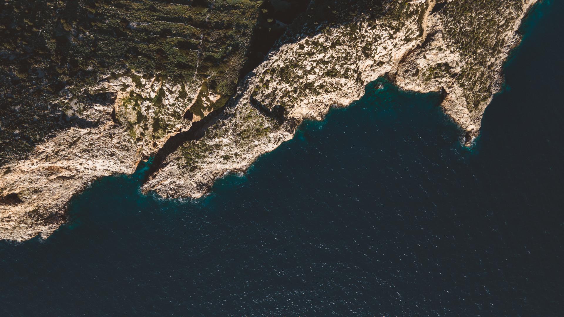 A stunning aerial view captures the rugged cliffs and blue sea along a natural coastline.