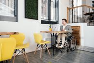 Woman in wheelchair browsing laptop in cafe