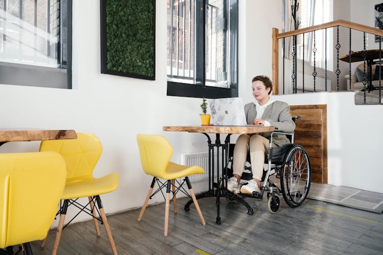 Woman In Wheelchair Browsing Laptop In Cafe