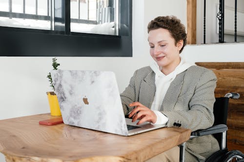 Cheerful woman in wheelchair working on laptop in cafeteria
